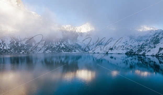 Mountains covered low clouds reflected in the clear lake – Stock photos from around the world